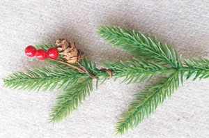 Detail of faux pine branch with green needles, red berries and a natural pine cone