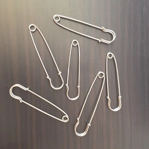 Detailed view of six silver stainless steel safety pins on a rustic wooden surface