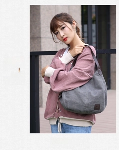 Gray canvas tote bag with brown leather straps worn by model on a city street