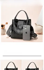 Detail of black glossy checkerboard bucket bag with wide woven strap and metal buckle