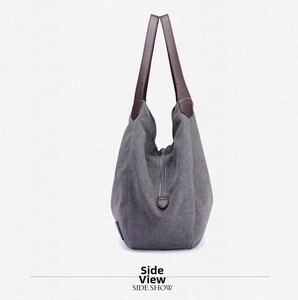Side view of dark gray canvas tote bag with brown leather handles and zipper detail