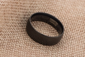 Detailed close-up of a black tungsten carbide ring showing clear internal engraving on fabric