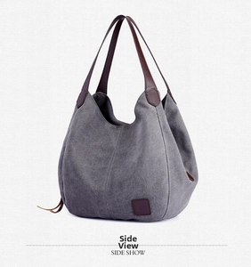 Side view of grey canvas tote bag showing dark brown leather handles and side strap detail