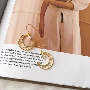 Dettaglio di orecchini a stella e luna dorati con cuore traforato su rivista di moda