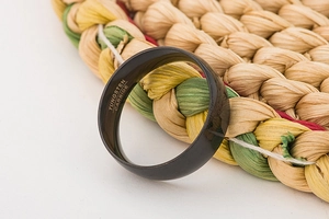 Close-up of 8mm black tungsten carbide ring with interior engraved lettering on woven mat