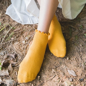 Yellow ribbed cotton ankle socks with frilly wood ear edges shown in a soft nature setting