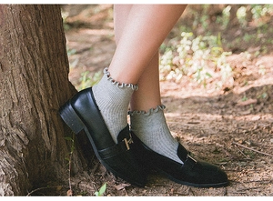 Close-up of women's grey cotton socks with ruffle cuffs paired with black leather loafers