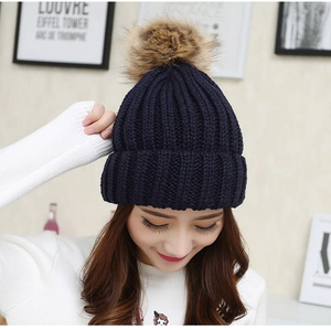 Close-up of a navy blue winter knit beanie featuring a large fluffy brown pompom top