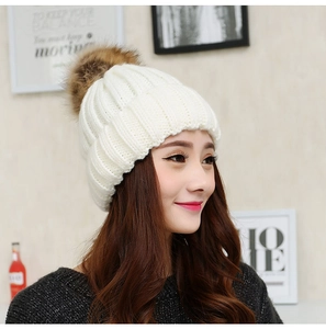 Profile view of a woman wearing a white cable knit beanie with a brown faux fur pom pom