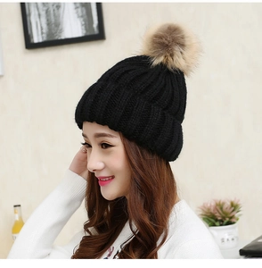 Detailed knit texture of a black winter beanie featuring a large brown faux fur pompom