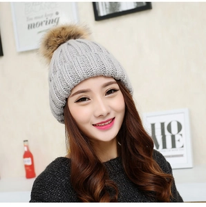 Close-up of light grey winter knitted beanie for women featuring a large brown faux fur pom