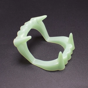 Close-up of glow-in-the-dark vampire fangs prop made of pale green luminous plastic material
