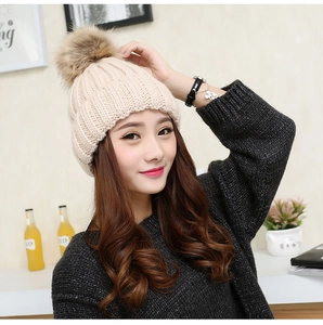 Close-up of beige knit beanie featuring a fluffy oversized faux fur pompom detail
