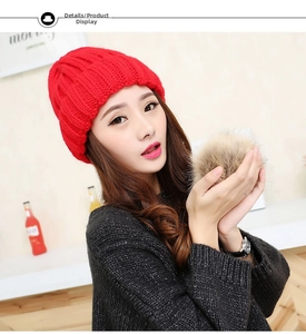 Close-up of red cable knit winter hat featuring a fluffy faux fur pom-pom detail