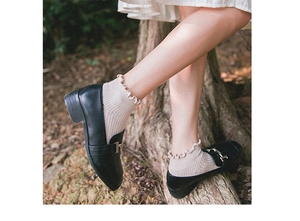 Close-up of beige cotton socks with ruffled edges worn with black loafers in forest
