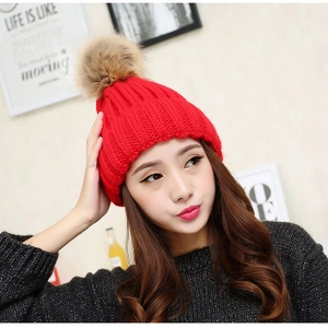 Detailed knit texture of red winter hat with a fluffy faux fur pompom decoration