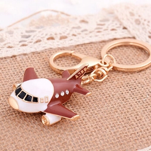 Porte-clés avion marron et blanc avec strass posé sur une toile de jute de couleur beige