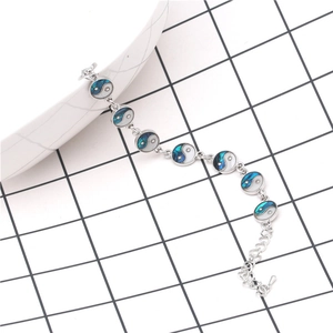 Silver Tai Chi Yin Yang bracelet with blue abalone shell inlay on white ceramic background