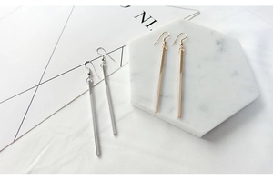 Macro shot of minimalist long bar geometric drop earrings in gold and silver finish