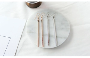 Minimalist long bar dangle earrings in gold and silver on white marble tray