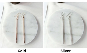 Detail of minimalist gold and silver long bar drop earrings on marble display