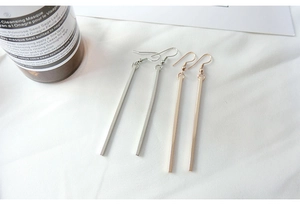 Close-up of minimalist silver and gold bar dangle earrings on a soft white cloth fabric