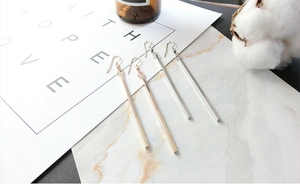 Close-up of minimalist long bar drop earrings in gold and silver on marble background