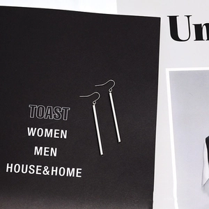 Detail shot of minimalist silver cylinder drop earrings on black display card