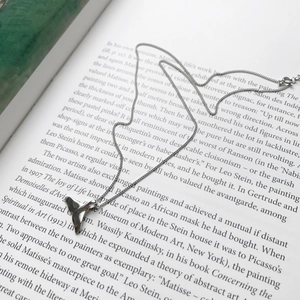 Detail of silver dolphin tail necklace resting on open book pages with soft lighting