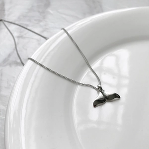 Polished 925 sterling silver whale tail pendant necklace displayed on a white plate