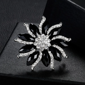 Silver flower brooch with black resin crystals on black leather texture background