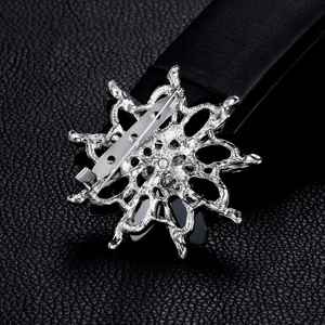 Silver flower brooch back view with metal pin on black textured leather background