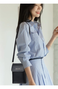 Side view of a black leather crossbody bag worn with a blue and white striped outfit