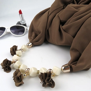 Detailed shot of brown fabric scarf with large square beads and floral pendant necklace
