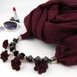 Detail of burgundy floral pendant scarf with metal buckle and beads on white background