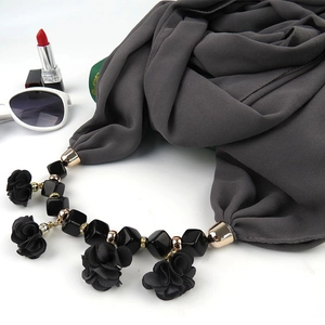 Detail of dark grey scarf with floral pendant and black beads on white background