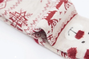 Macro shot of knit beige Christmas socks featuring red reindeer patterns and soft textures