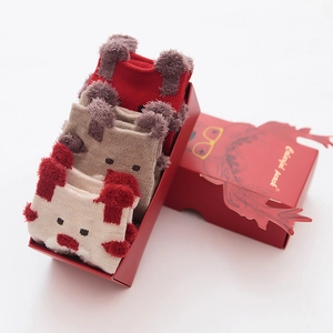 Three pairs of Christmas plush socks in a festive red reindeer gift box on white background
