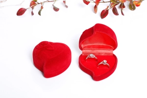 Detail of red heart-shaped velvet jewelry box featuring two silver rings on white background