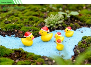 Miniature yellow Christmas duck figurines with red hats on moss landscape