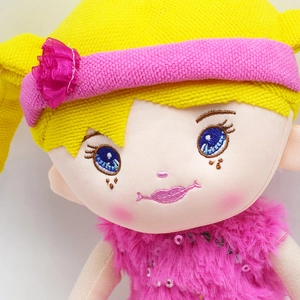 Close-up of cute plush doll with blue embroidered eyes and pink sequin dress details