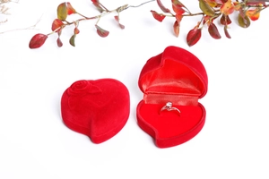 Close-up of a red heart-shaped velvet jewelry box featuring rose relief and a silver ring