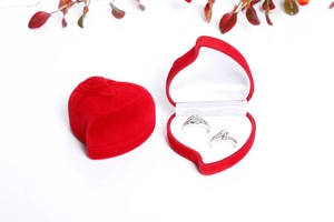 Detail of red heart velvet jewelry boxes with rose relief and silver rings inside