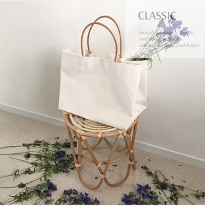 Minimalist white canvas tote bag with round wooden handles placed on a woven stool