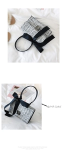 Detail of tweed square handbag with a large black bow and metallic clasp on fabric
