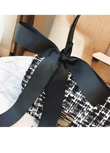 Close-up of black and white tweed handbag featuring a large elegant bow and metal buckle