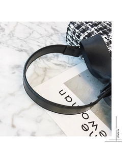 Close-up of black and white tweed handbag with leather strap and bow detail