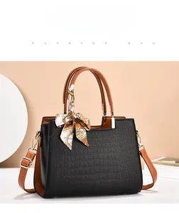 Detail of black crocodile texture handbag with contrast brown handle and decorative silk scarf