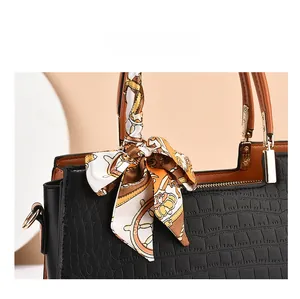 Close-up of black crocodile embossed handbag featuring a floral silk scarf handle detail