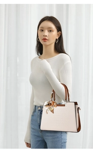 Detail of beige crocodile pattern handbag with caramel trim and yellow scarf accent